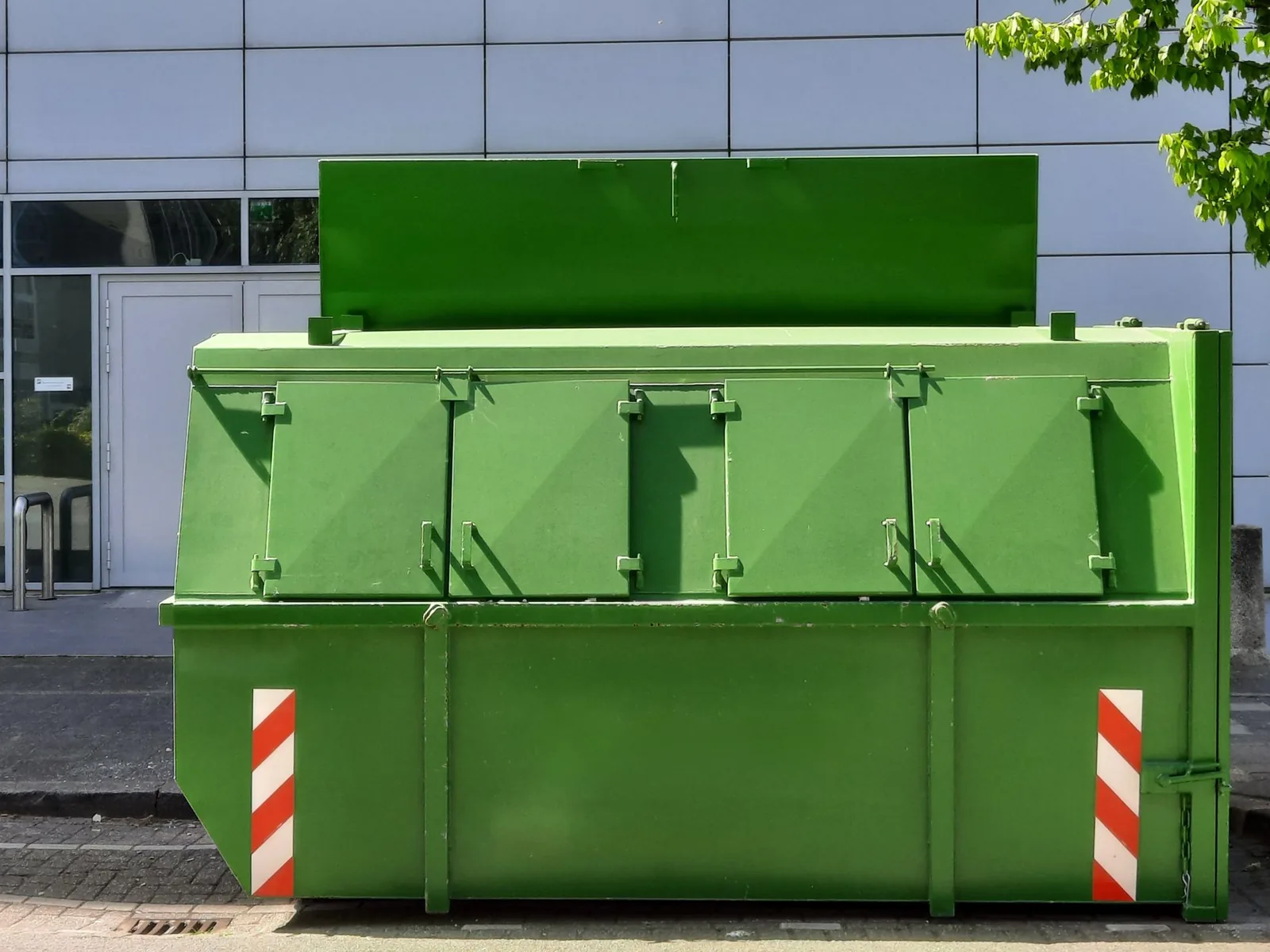 Una volqueta verde con franjas reflectivas en la vereda, frente a un edificio